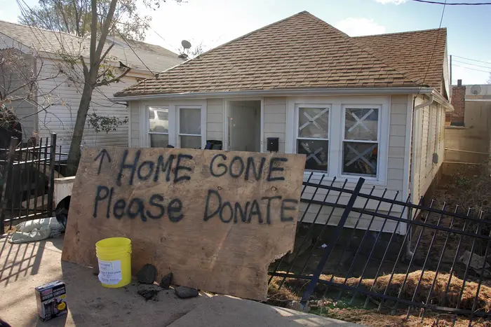 A large sign in front of a boarded up home reads: “Home Gone Please Donate.”